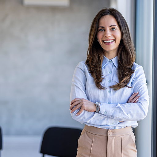 A woman in a light blue shirt and beige trousers standing with her arms folded in an office