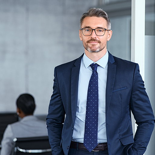 A man wearing glasses and a dark navy suit standing in an open-plan office