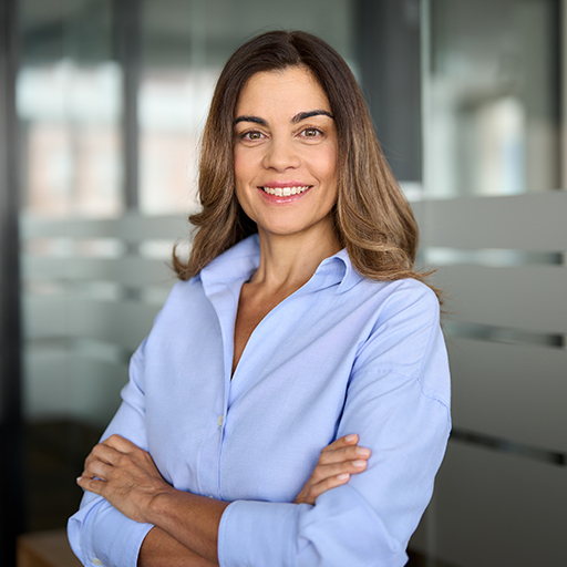 A woman in a pale lilac shirt standing with her arms folded in an office