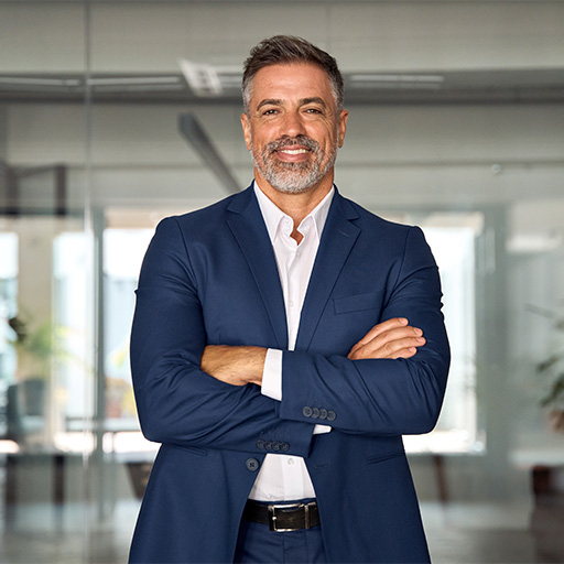 A man in a navy suit standing with his arms folded in a bright office