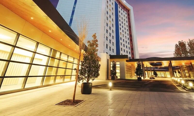 Modern hospital building at dusk with illuminated entrance and clock tower.
