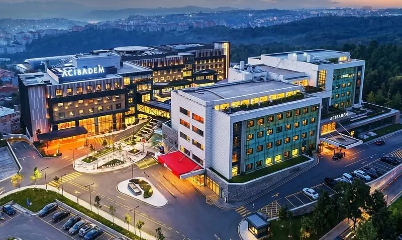 Aerial view of Acibadem Maslak Hospital at sunset with cityscape background.
