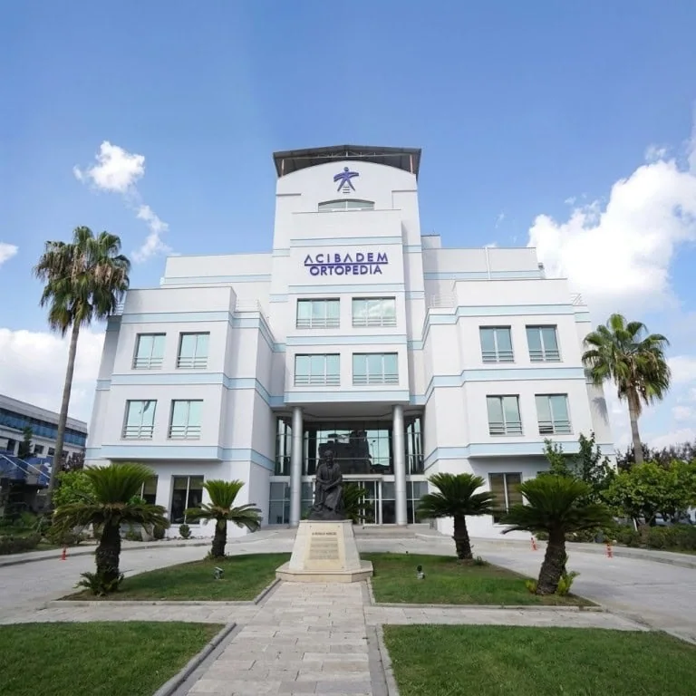 Modern Acibadem Orthopedia Hospital with palm trees and blue sky.