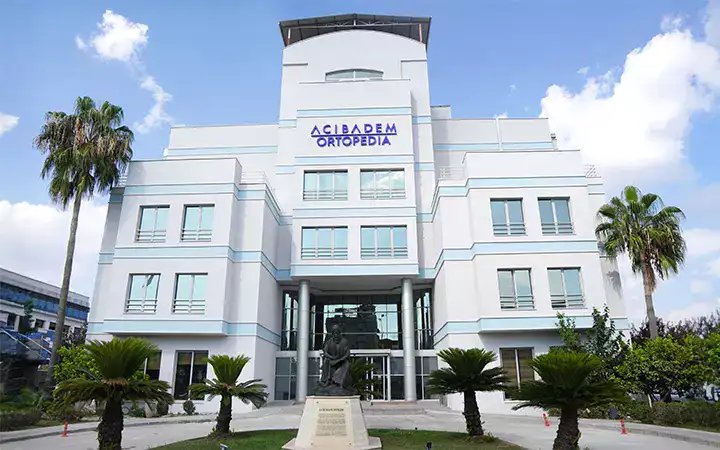 Modern Acibadem Orthopedics Hospital building with palm trees, white facade, and clear sky.
