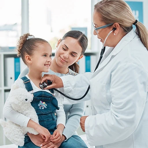 A doctor listening to a young girl's chest with a stethoscope while her mother holds her, at a children's health check-up