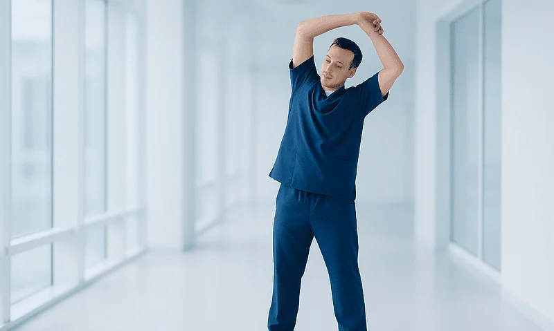 Male healthcare worker stretching in hospital corridor after knee replacement.