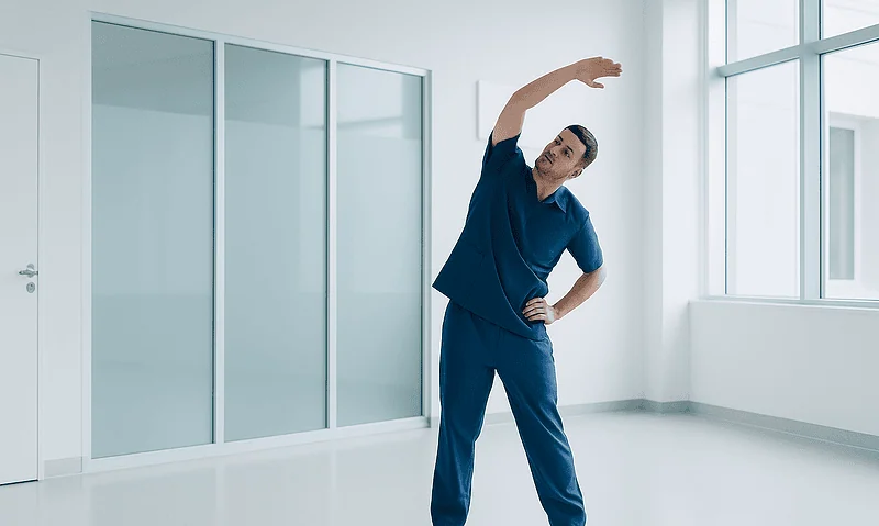 Male healthcare professional stretching in a modern hospital room.